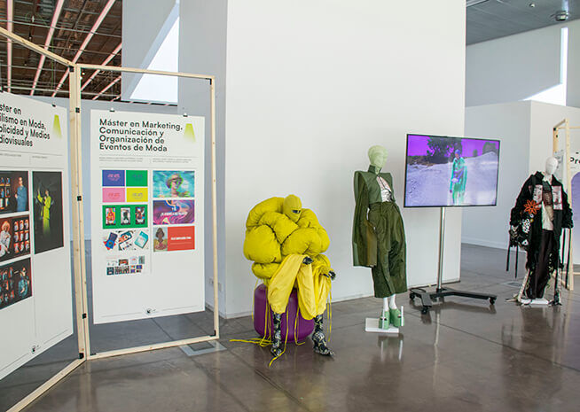 Espacio de exposición que muestra un máster en marketing de moda, con maniquíes vestidos con atuendos modernos y una pantalla informativa.