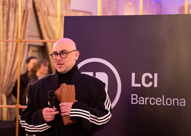 Un ponente en un evento de LCI Barcelona con un micrófono y un premio de madera, listo para dirigirse al público.