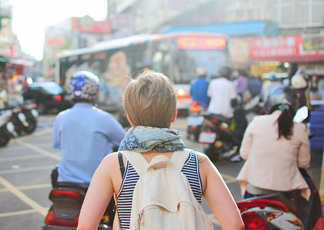 Una mujer mira hacia adelante en una calle urbana bulliciosa, rodeada de motocicletas y un autobús, personificando el ritmo dinámico de la vida en la ciudad.