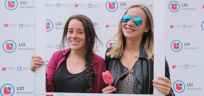 Dos mujeres jóvenes sonrientes en un evento al aire libre, una con un helado.