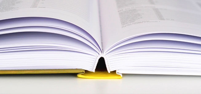 Un libro de tapa dura con páginas blancas yace abierto sobre una mesa, con el lomo apoyado en la cubierta amarilla.