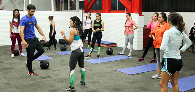 Un grupo mixto se involucra en una clase de fitness interior, enfocándose en movimientos funcionales.
