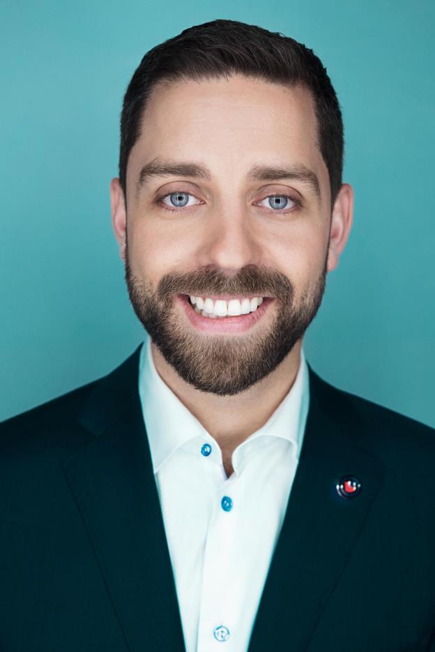 A bearded man with blue eyes, wearing a navy blazer and a white button-up shirt.