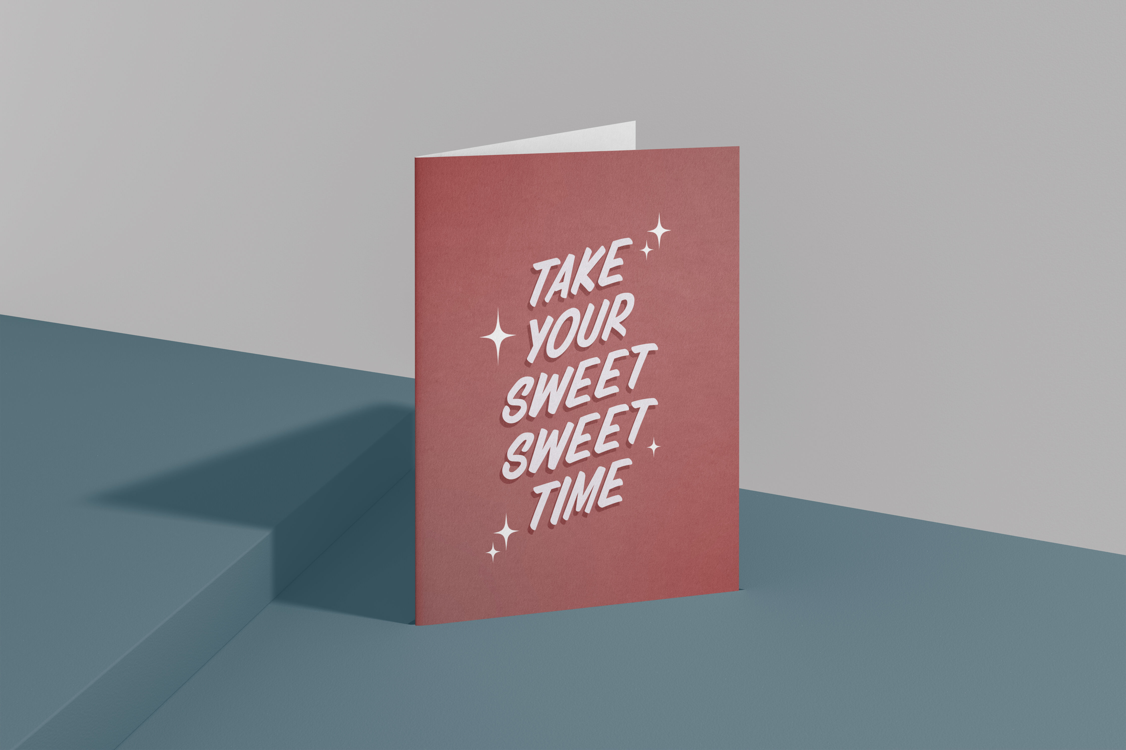 A red greeting card stands on a blue surface, inscribed with "TAKE YOUR SWEET SWEET TIME" in white, sparkly lettering.