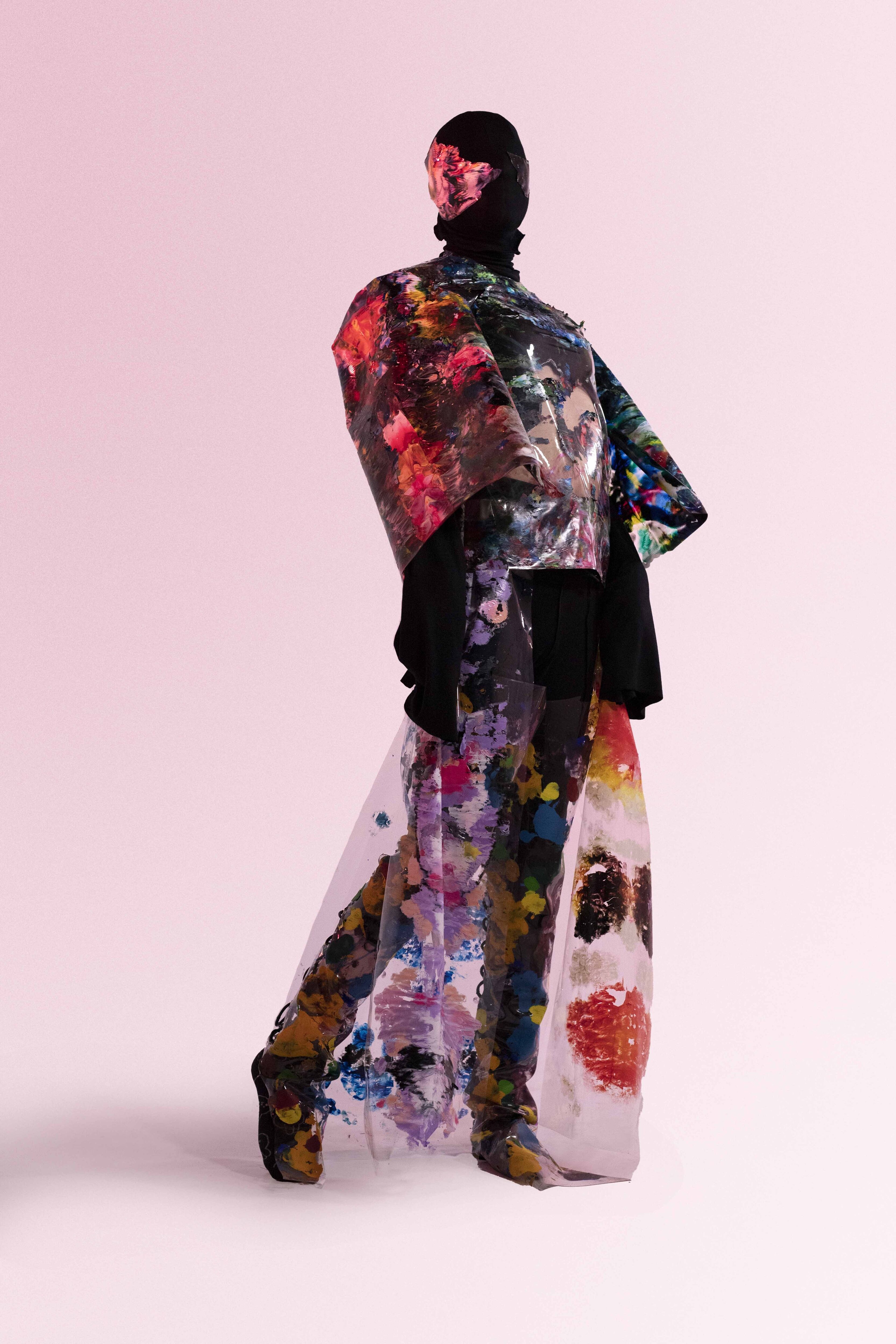 A person models a translucent, floral-painted cloak against a pink backdrop.