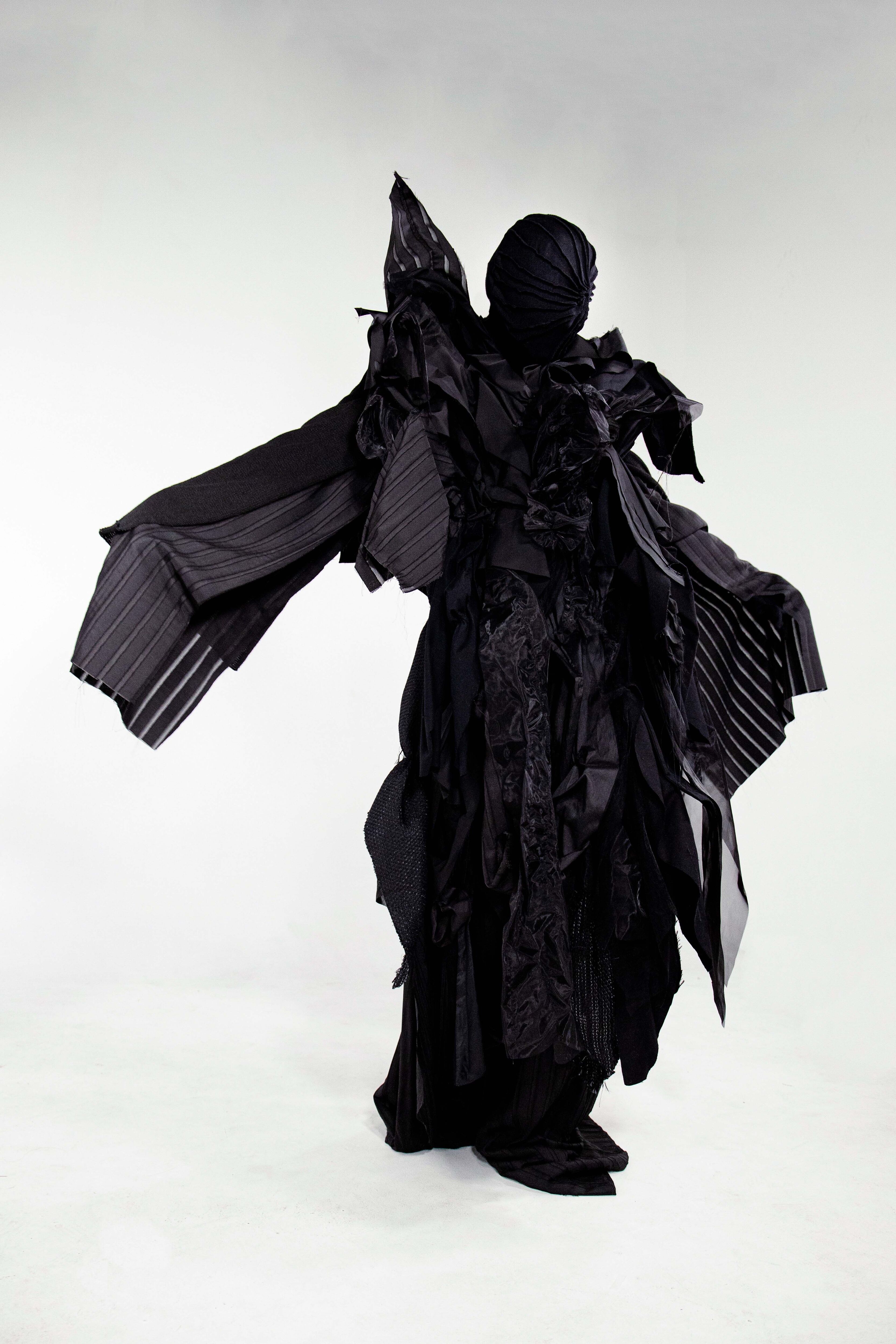 An individual shrouded in a voluminous black fabric outfit, presenting a dramatic and artistic silhouette with hidden features.