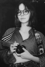 A young woman in retro glasses and patterned clothing holds a classic camera, exuding a nostalgic charm.