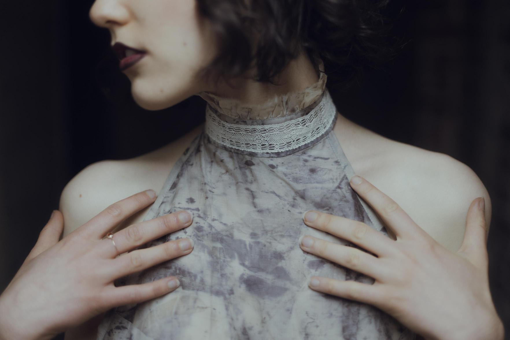 A close-up of a woman adorned with a delicate lace collar, her hands gracefully resting on a textured garment.