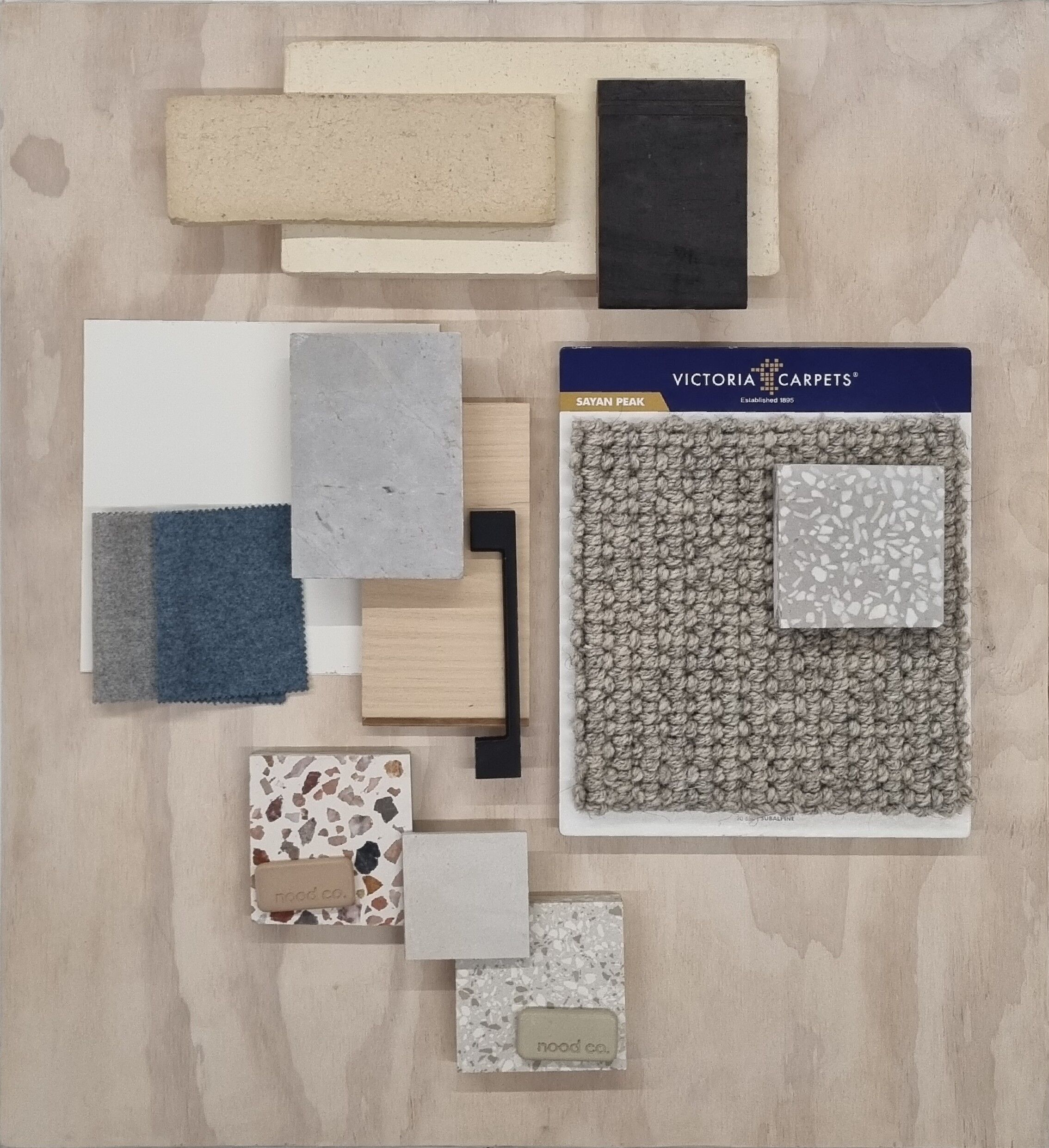 An arrangement of interior design samples including various tiles, woods, and carpet textures on a wooden surface.