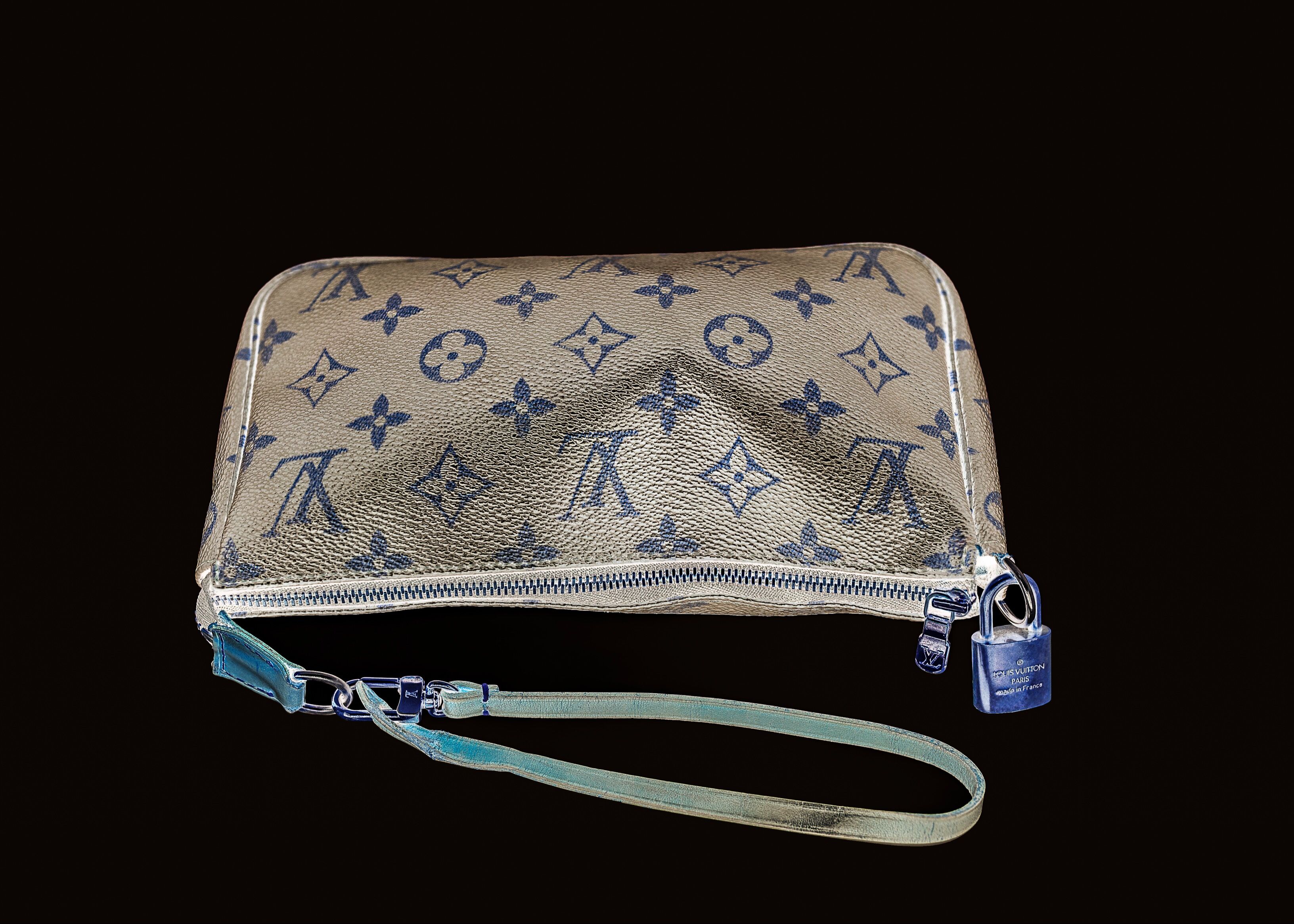 A luxury branded cosmetic pouch with a monogram print and an attached blue padlock, against a black background.