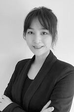 A monochrome photograph captures a young woman with a pleasant smile, dressed in a business suit, exuding confidence.