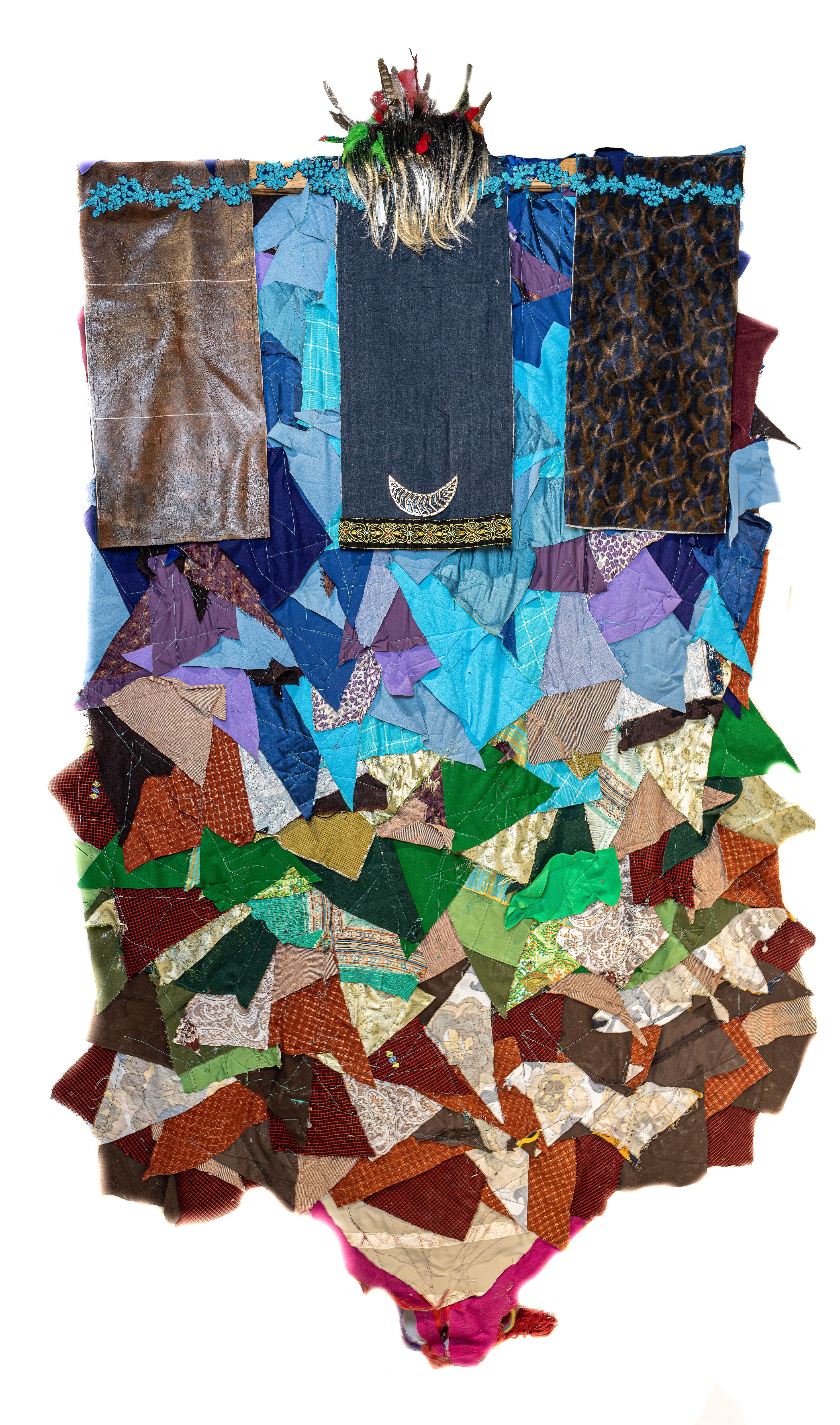 A vertical collage of triangular textile pieces in varied colors, topped with a section of leather and dark denim, adorned with a crescent emblem and a fur headdress.