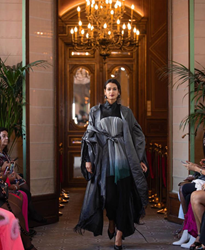 A model strides confidently through a grand hallway, her flowing dark ensemble a modern twist on classic couture.