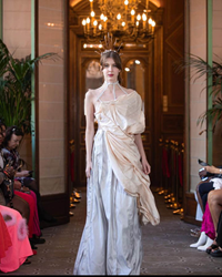 Draped in a flowing gown with ethereal layers, the model exudes a timeless grace in the grand hallway.