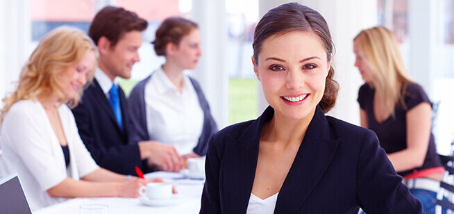 Una mujer segura lidera una reunión de negocios, su presencia atractiva ejemplifica cualidades de liderazgo mientras se dirige a sus colegas en un entorno de oficina luminoso.