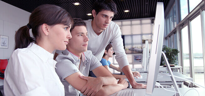 Un equipo de profesionales de tecnología trabaja colaborativamente en un proyecto, enfocados profundamente en sus pantallas de computadora en un entorno de oficina moderno.