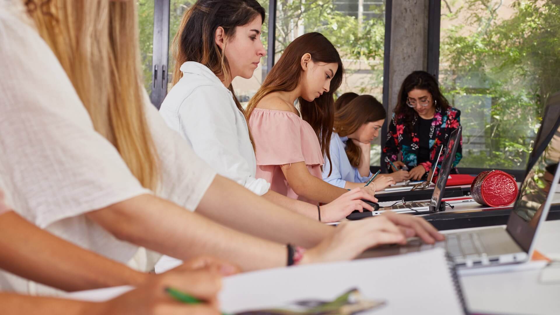 Un grupo de estudiantes femeninas enfocadas trabajando colaborativamente en sus tareas en un aula bien iluminada, representando el trabajo en equipo y la dedicación.