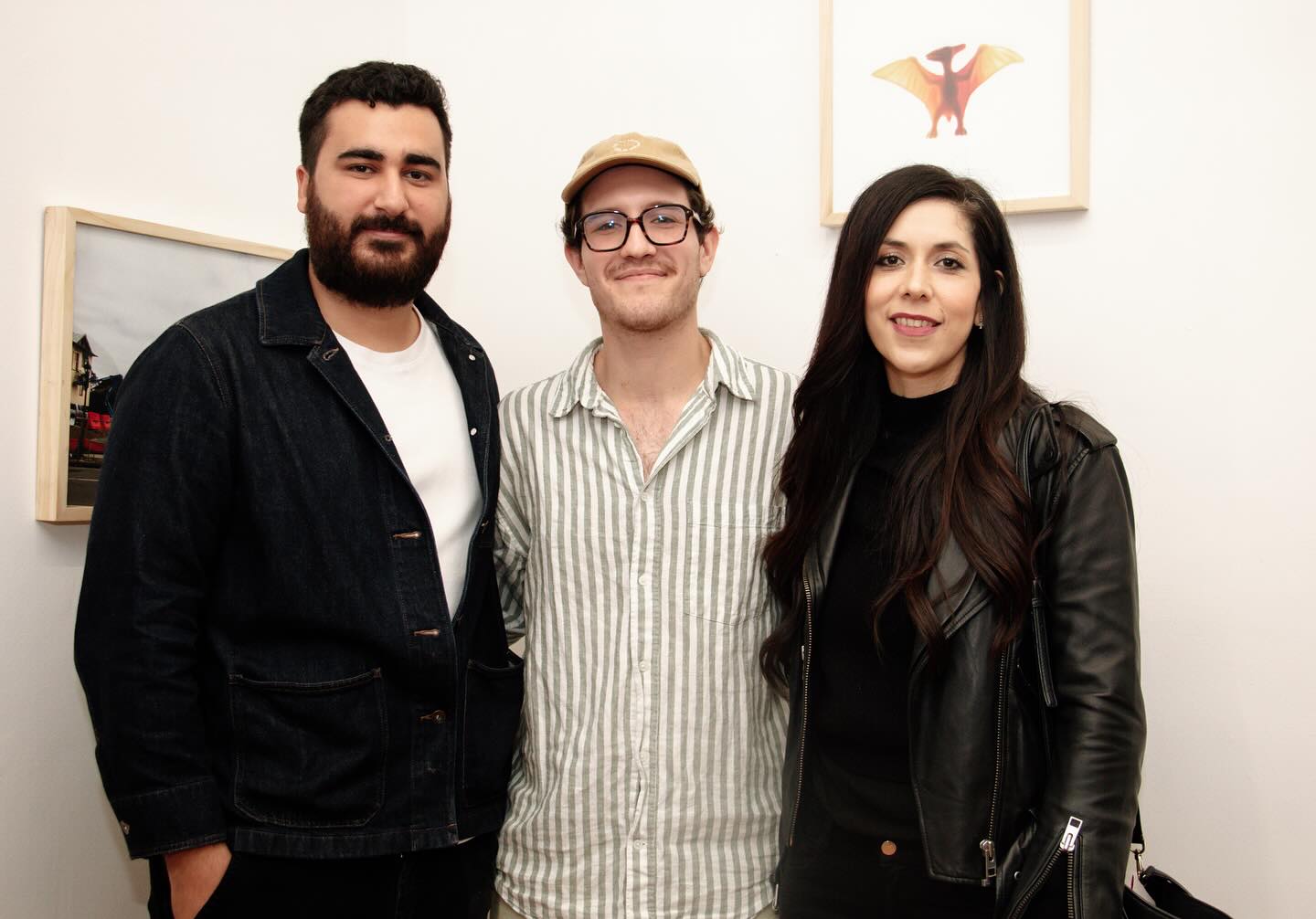 Una reunión alegre de tres personas posando juntas frente a una obra de arte en una galería de arte, destacando su disfrute colectivo de las artes.