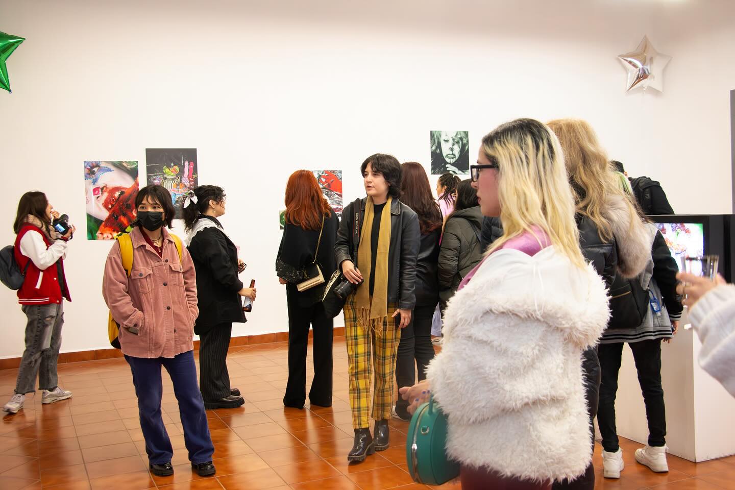 Visitantes de diversos estilos y orígenes entablan conversaciones en una exposición de arte vibrante, rodeados de diversas obras de arte.