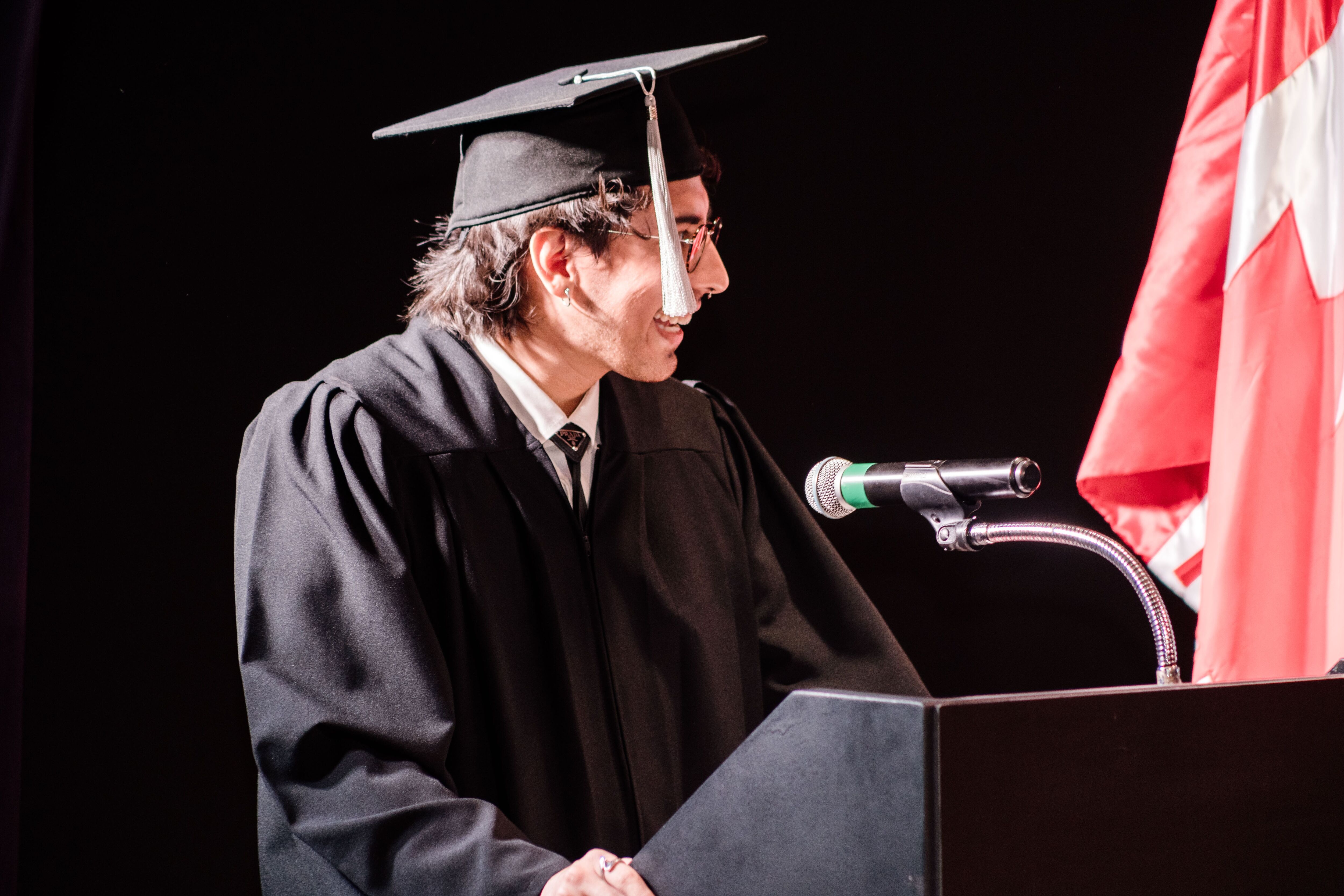 Un graduado entrega alegremente un discurso de apertura en una ceremonia de graduación, vestido con el atuendo académico tradicional y exudando confianza.