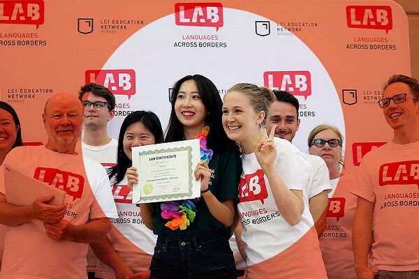 A diverse group of people in red shirts, celebrating a woman holding a certificate, at a "Languages Across Borders" event.