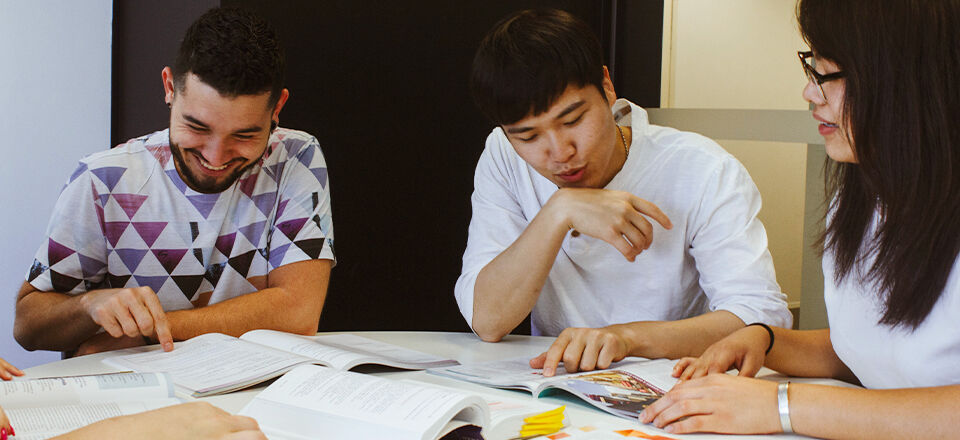 Three people engaged in a study session, with open books on the table, sharing a light-hearted moment.