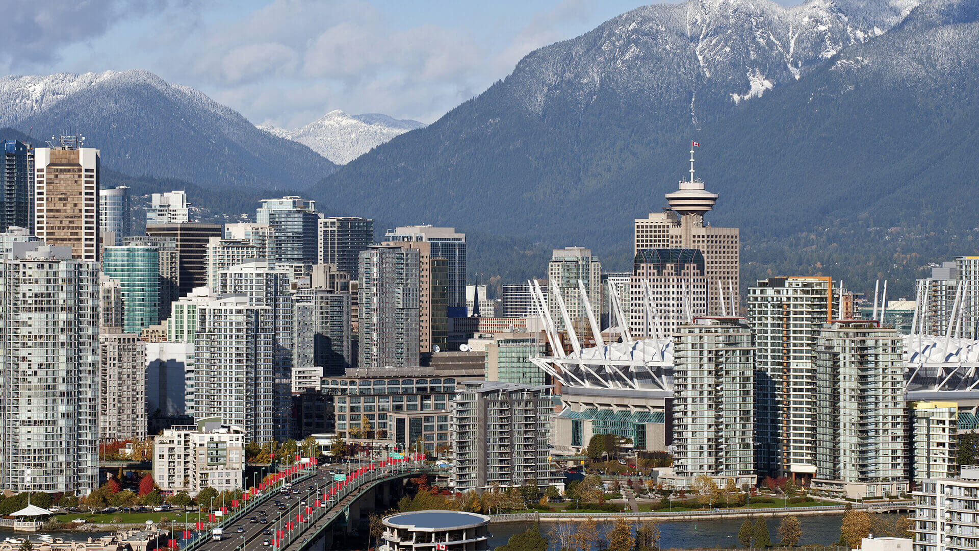 A panoramic view of Vancouver's modern skyline, with the iconic Harbour Centre and snow-capped mountains in the background.